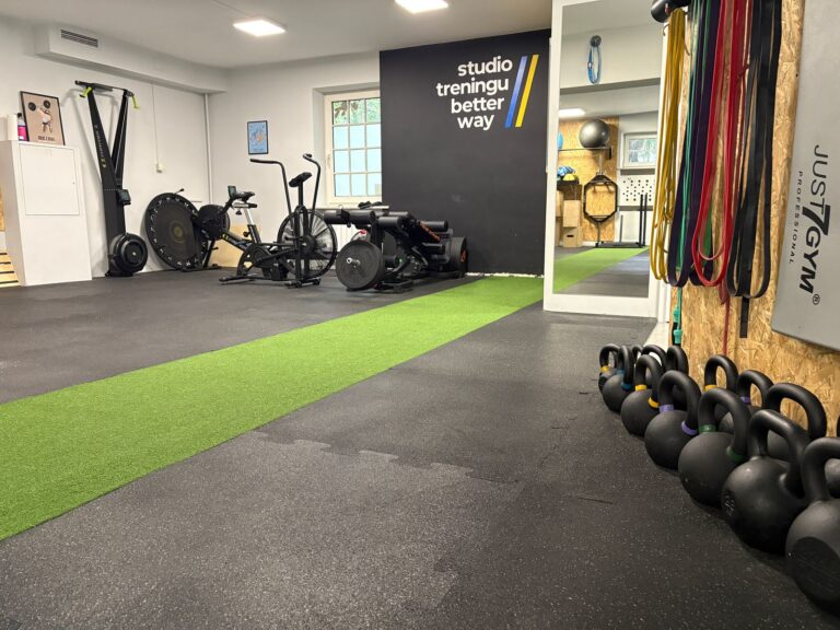 Sala Studio Treningu Better Way w Konstancinie-Jeziornie: ściana z logo, rowery powietrzne, kettlebelle i tor ze sztucznej trawy